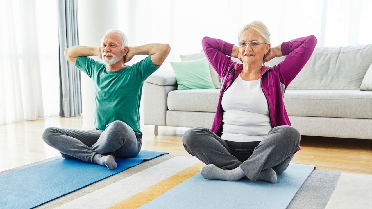 senior couple sit on yoga mats doing a stretch, with hands behind their heads