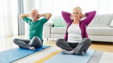 senior couple sit on yoga mats doing a stretch, with hands behind their heads
