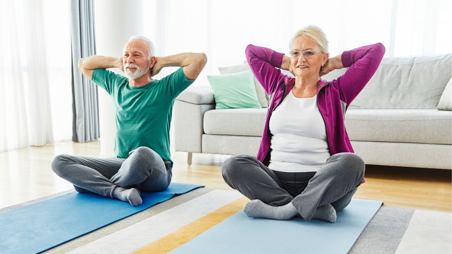 senior couple sit on yoga mats doing a stretch, with hands behind their heads