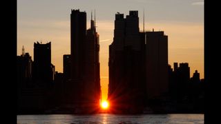 The sun rises over 42nd street behind the skyline of midtown Manhattan during a reverse Manhattanhenge sunrise in New York City