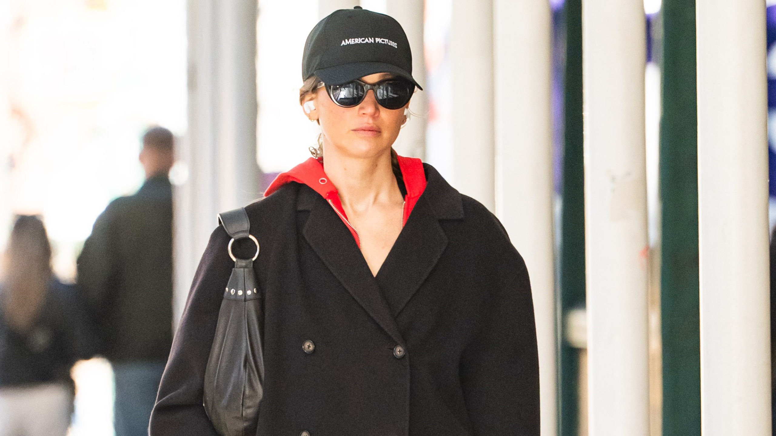 Jennifer Lawrence wears a baseball cap, red sweatshirt, and chocolate-brown jacket.