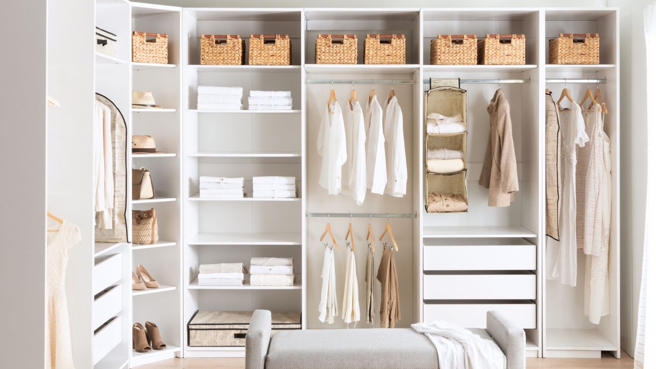 Open shelving and closet system on left and back wall pictured. Very neat, tidy and uncluttered with wicker baskets along the top, matching wooden hangers and no overcrowding of neutral items on rails