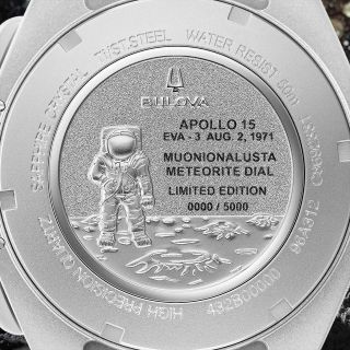 closeup of the silver metallic back of a watch, which shows an engraving of an astronaut on the moon's surface.