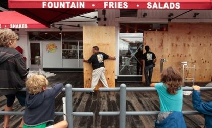 Children watch workers remove plywood from a restaurant in lower Manhattan Sunday: The hurricane may provide some temporary clean-up work, but tourism also took a hit.