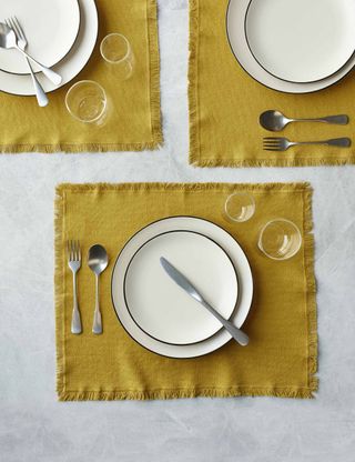 mustard yellow placemats with plates and cutlery set out on top