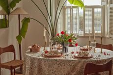 A circular dining table with a floral tablecloth, a centerpiece of red and green flowers, and Easter themed decorations including bunny ear napkin rings
