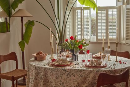 A circular dining table with a floral tablecloth, a centerpiece of red and green flowers, and Easter themed decorations including bunny ear napkin rings