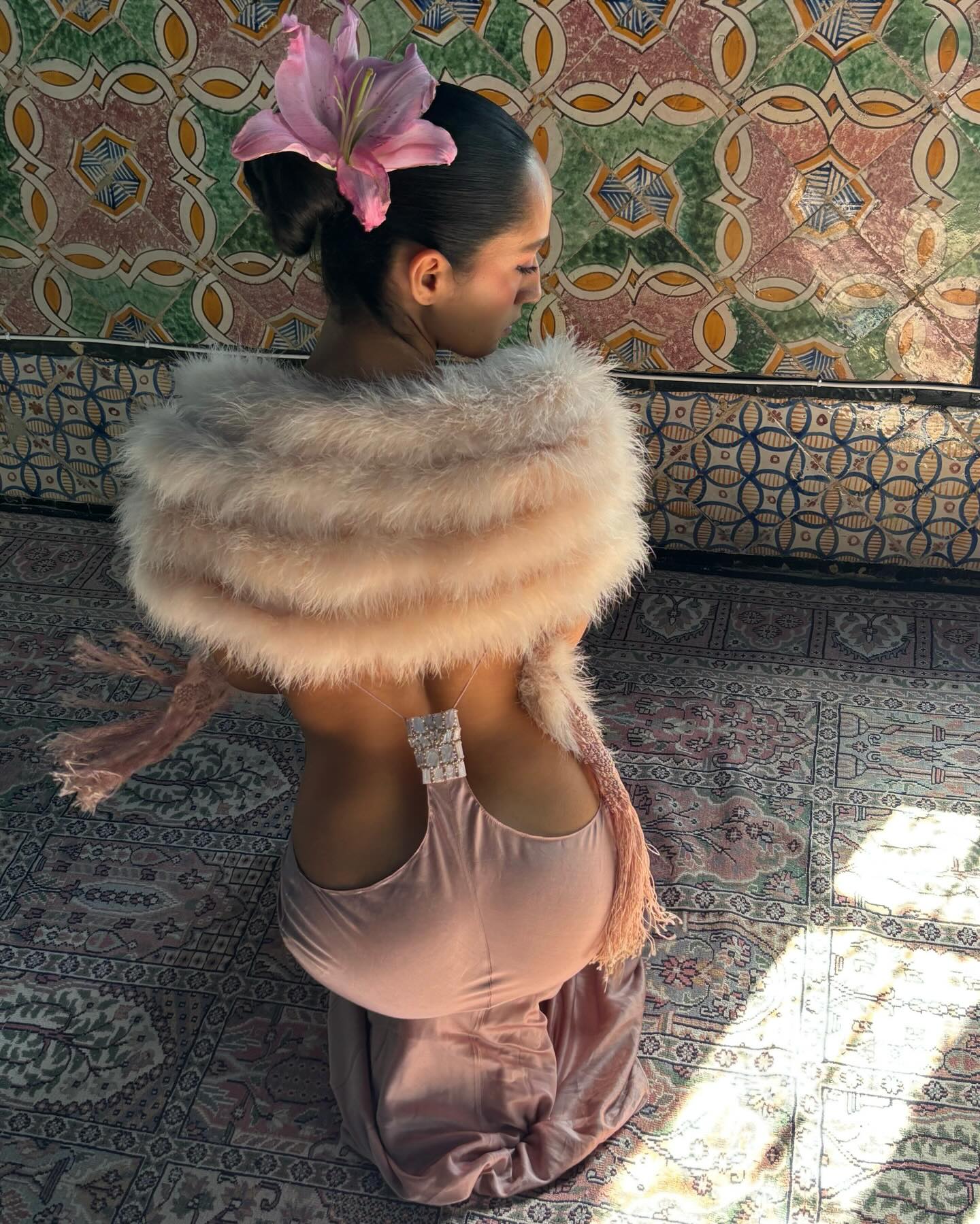 An image of a woman with a pink dress on, a fur shawl, and a flower in her updo.