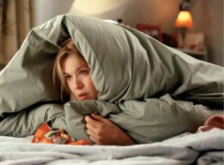 Bridget Jones hides under a blanket with candy wrappers