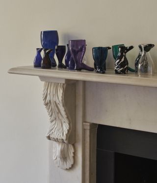 The living room mantelpiece clinks with a clutch of precious glass boots