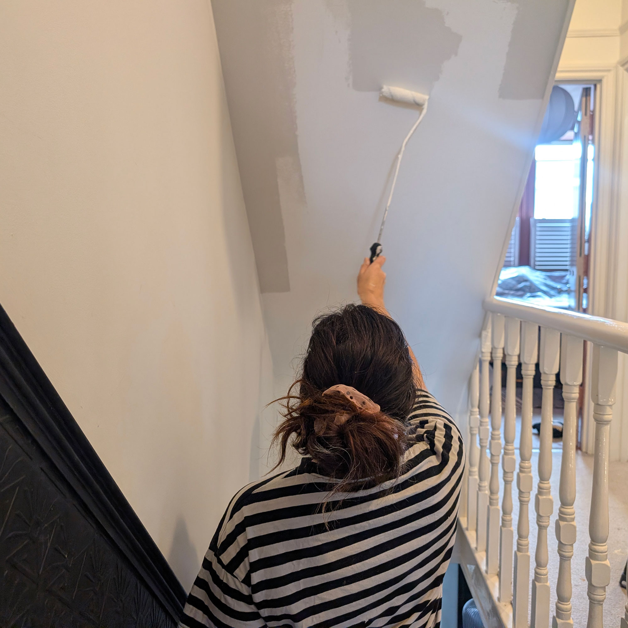 Woman painting ceiling above staircase white with a paint roller