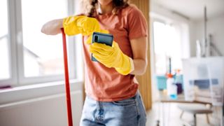 Woman holding a smartphone wearing washing up gloves