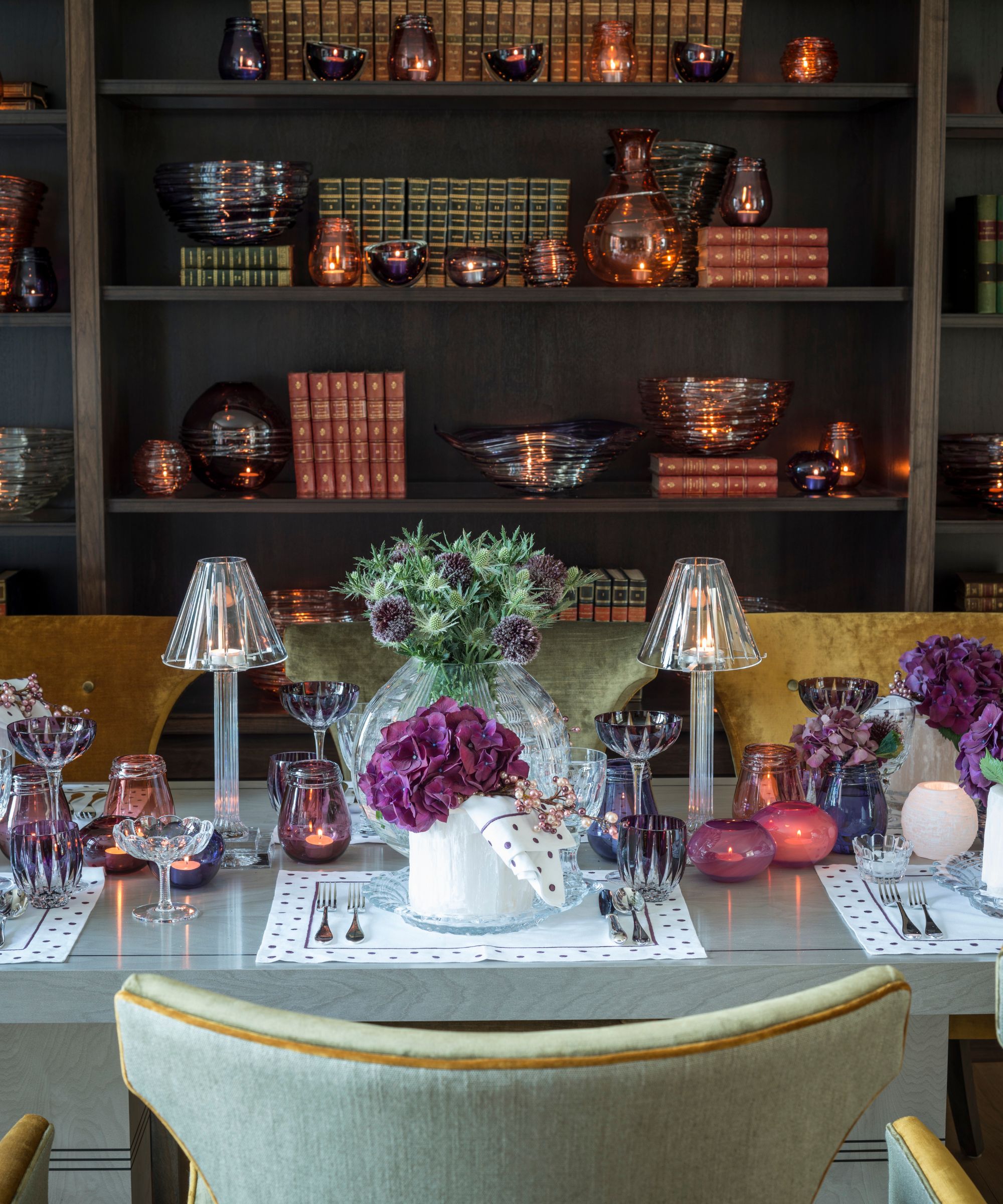 Dining table with purple glassware, hydrangeas and a styled bookshelf in the backrgound
