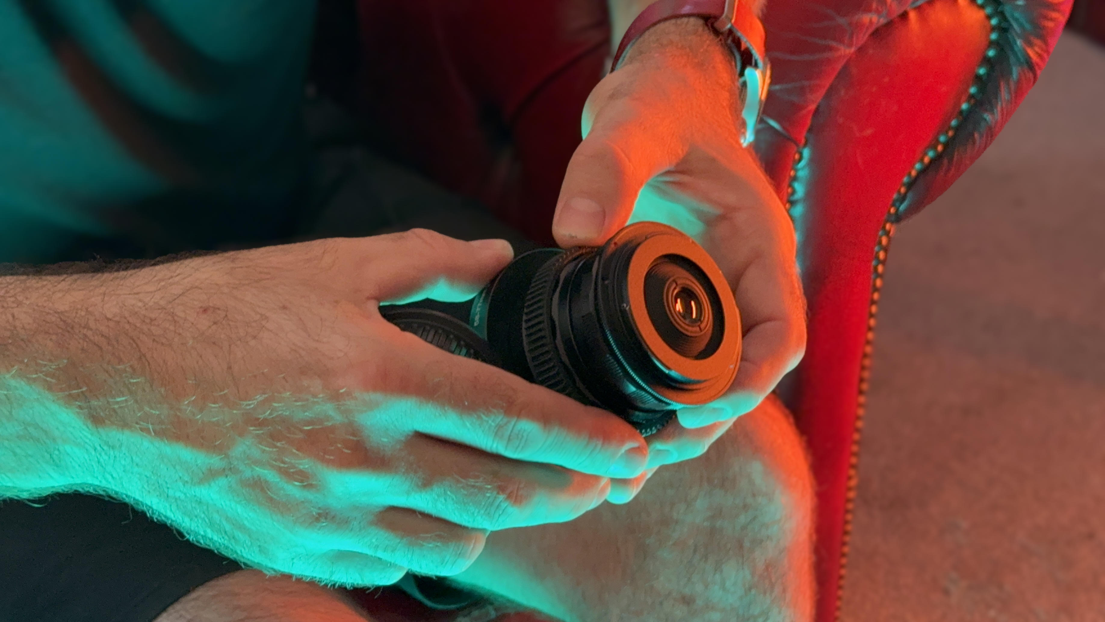 A person handling a camera lens lit by a red light