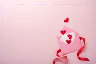 A pink envelope with a red ribbon and hearts on a pink background