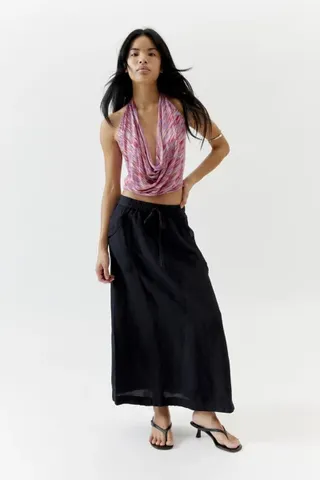 seorang model mengenakan rok midi linen hitam dengan tank top berwarna merah muda