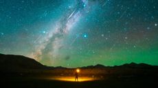 A stargazer standing on a plain with many shooting stars streaking overhead
