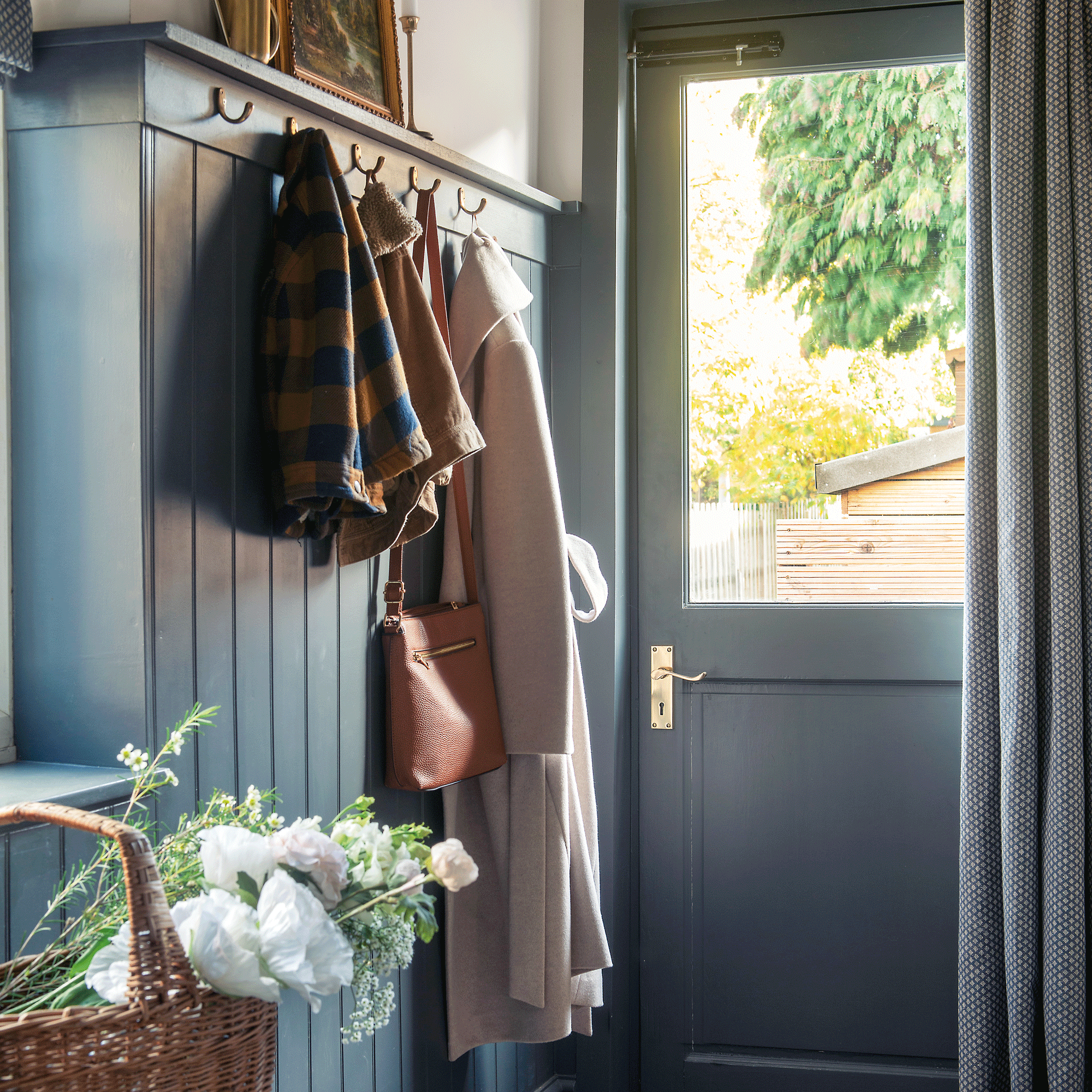 a hallway with dark blue panelled walls a coat rail and a door curtain beside a half glazed back door