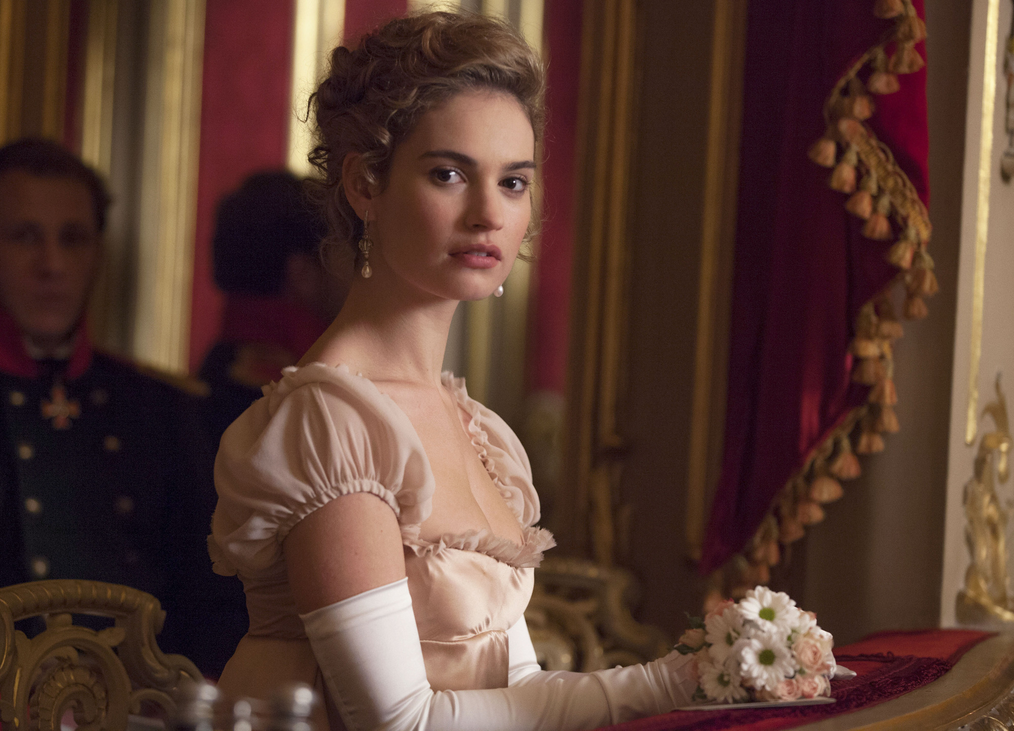 Lily James as Natasha wearing a pink dress and holding flowers.