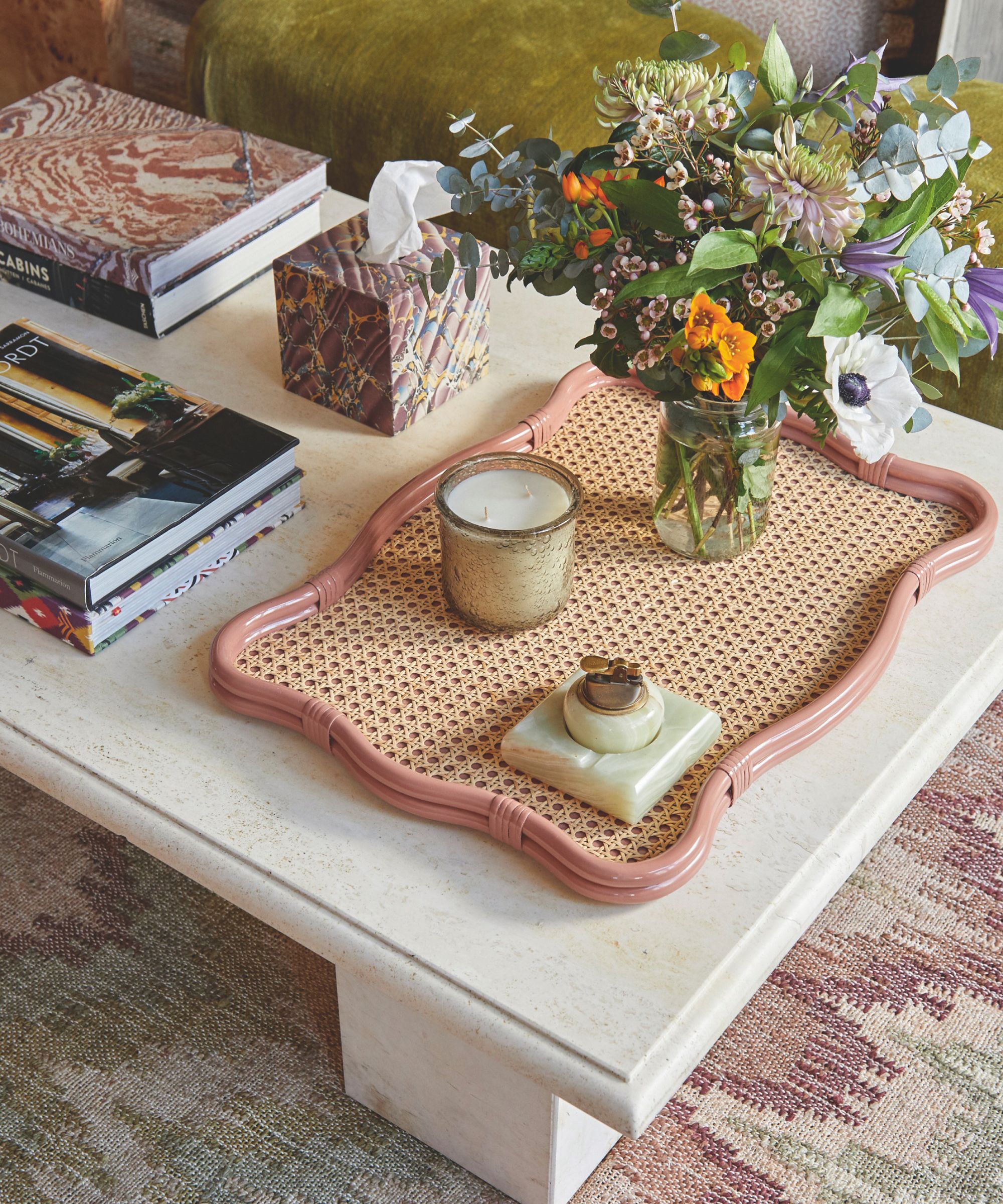 A close up of a white marble coffee table with a pink wavy tray and items on the tray including a jar of flowers, a candle and an ornament