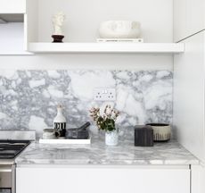 A white kitchen countertop with a marble backsplash and housing decorative bowls, a pestle and mortar and a small vase of flowers