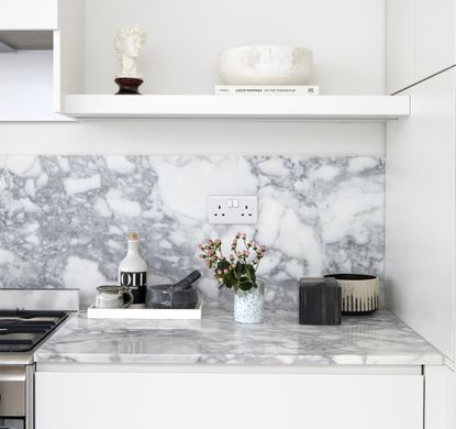 A white kitchen countertop with a marble backsplash and housing decorative bowls, a pestle and mortar and a small vase of flowers