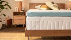 Tempur-Pedic mattress topper om a bed; to the left, a lamp on a wooden nightstand against cream walls.