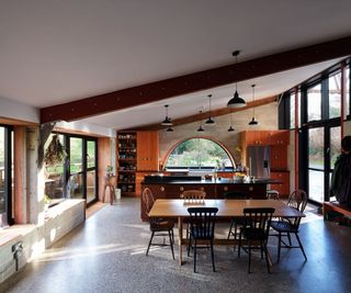 An open plan kitchen with windowed walls, kitchen island and dining table
