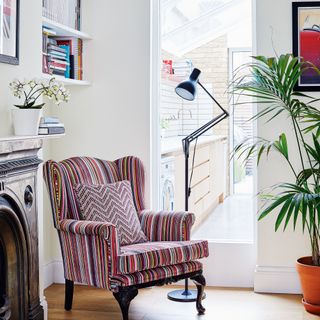 living room with upholstered striped armchair Anglepoise lamp fire surround shelving and a glass window through to the kitchen