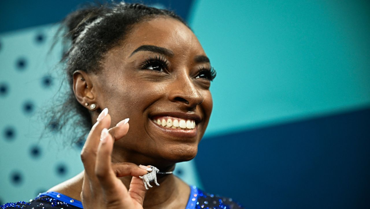 Simone Biles holds up a diamond goat necklace after winning the women&#039;s all around gymnastics final in Paris