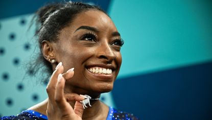 Simone Biles holds up a diamond goat necklace after winning the women&#039;s all around gymnastics final in Paris