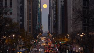 the full moon can be seen above a busy street between two rows of large buildings in a crowded city