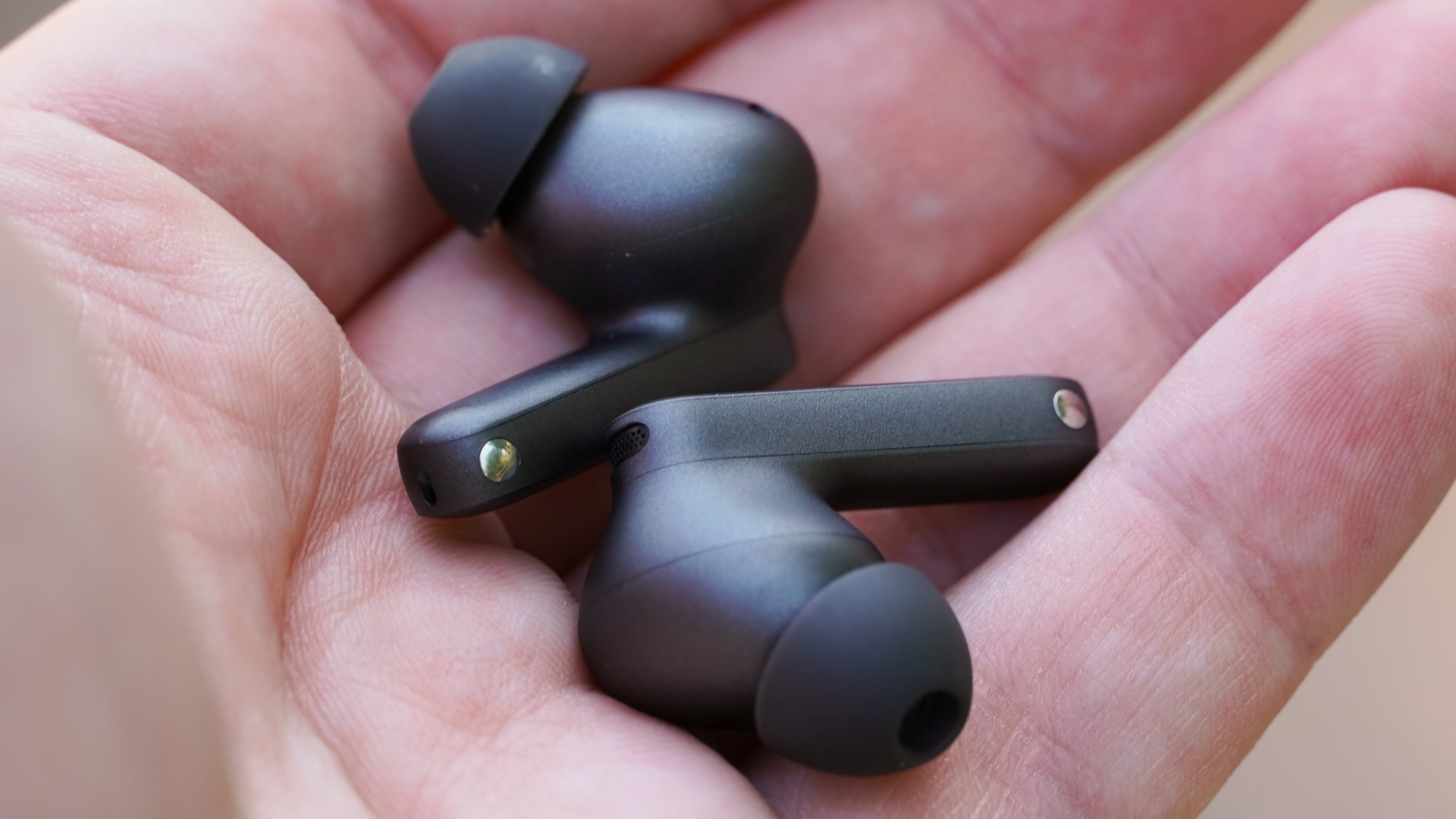 The OnePlus Buds 4 in Storm Gray in the palm of my hand.