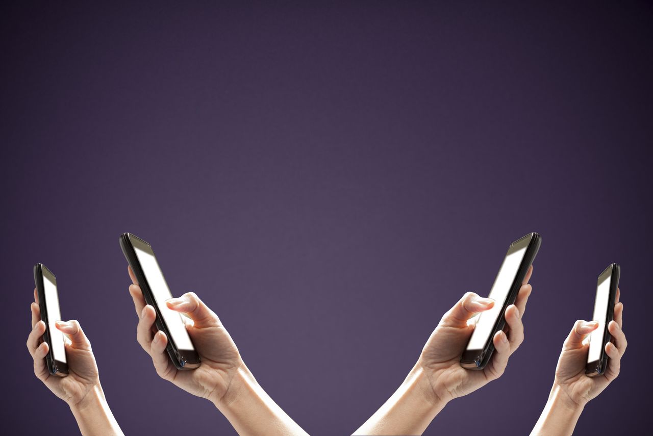 Four identical hands holding up smart phones on purple background