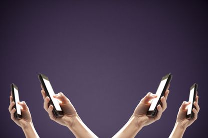 Four identical hands holding up smart phones on purple background