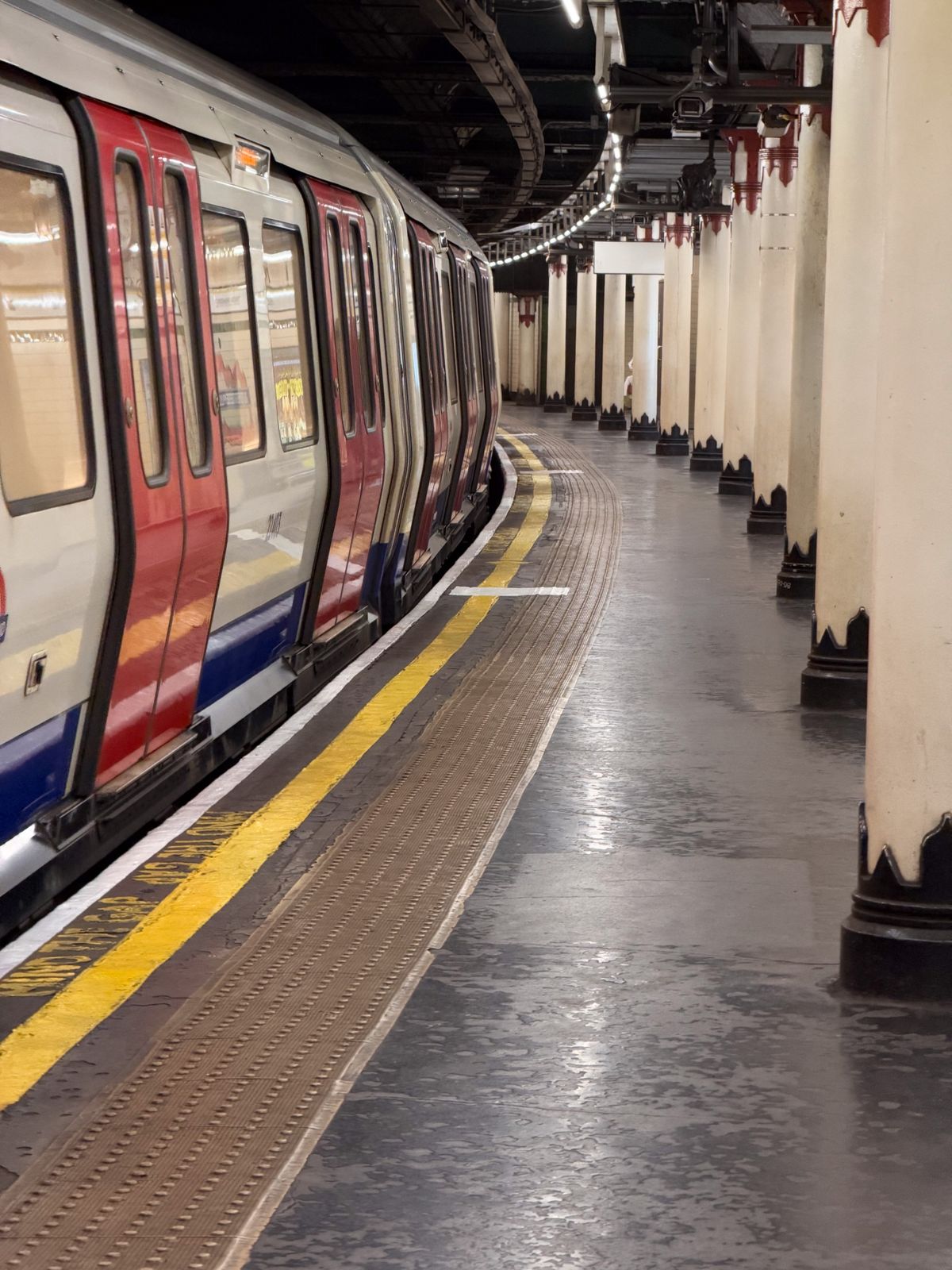 London Underground train standing beside a curved platform lined with cream columns and a yellow safety line.