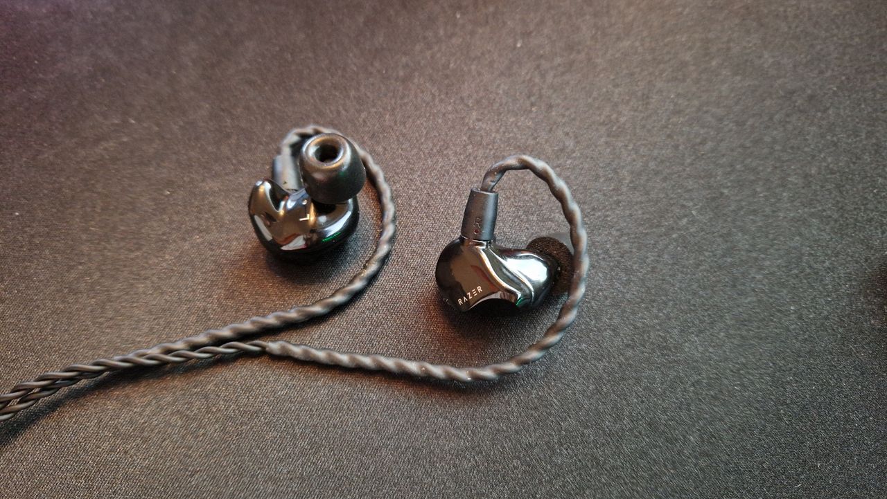 Razer Moray review image Of the earbuds lying on a desk mat with the left earbud facing upward