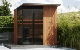 wooden and glass sauna building on patio with planting to side and rear