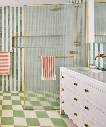 A bathroom with a chequered green and off-white tiled flooring and striped green and off-white tiled walls