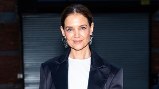 Image of Katie Holmes smiling with brunette ponytail and wearing a white T-shirt and satin navy blazer