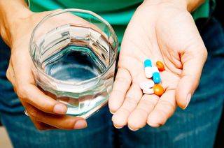 A woman holds a handful of pills and a glass of water.