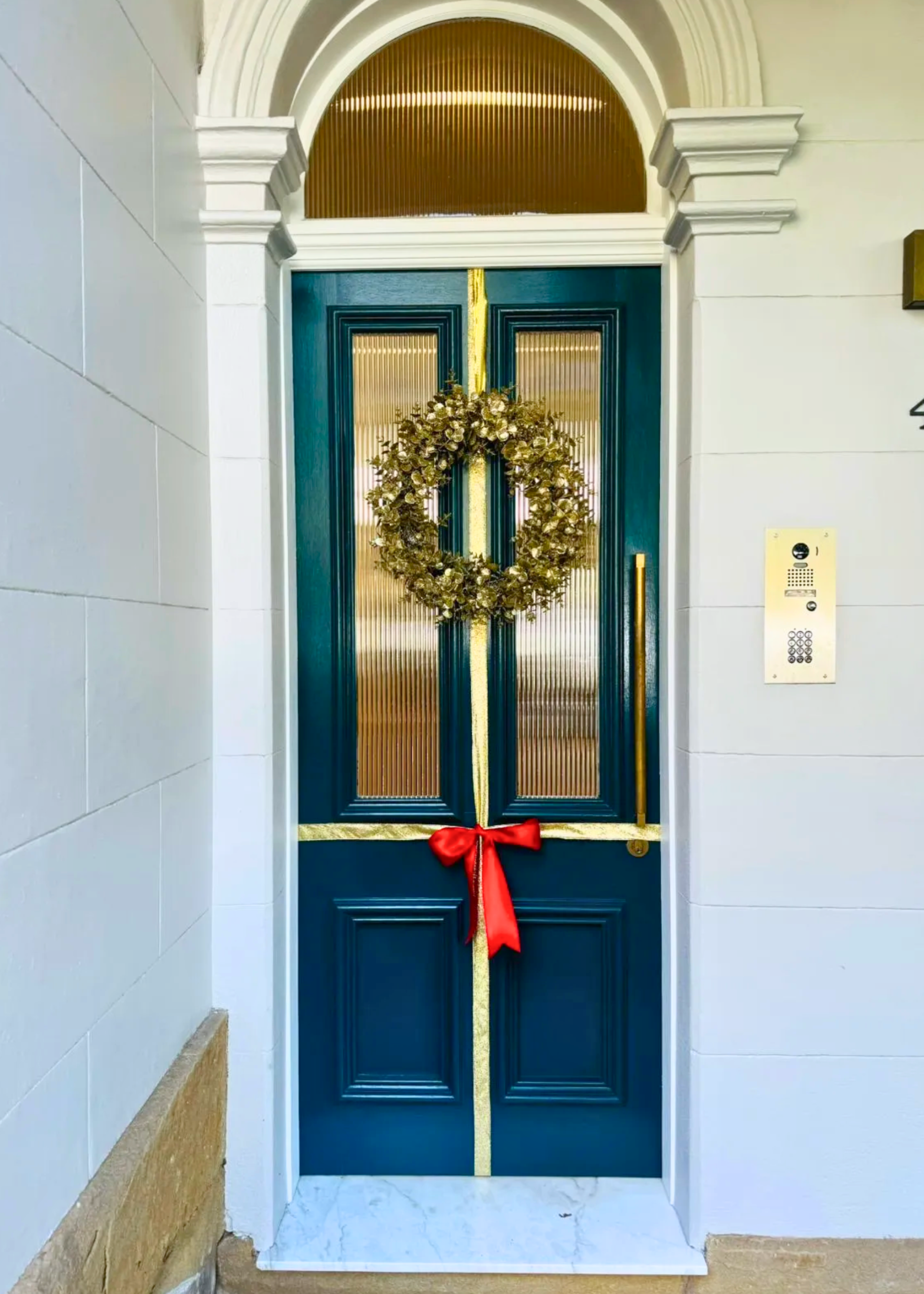 A teal colored front door decorated with gold ribbon like a christmas present with a red bow in the middle and a gold wreath hanging at the top