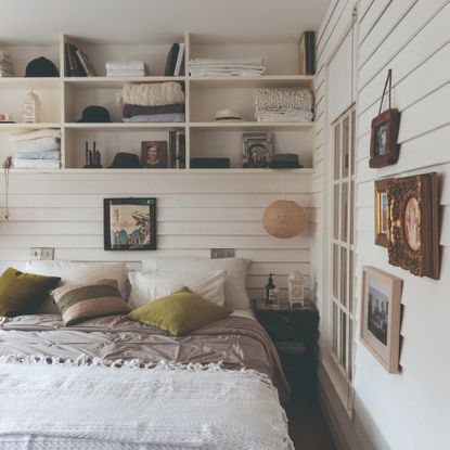 A white bedroom with panelled walls with open shelving and a gallery wall 