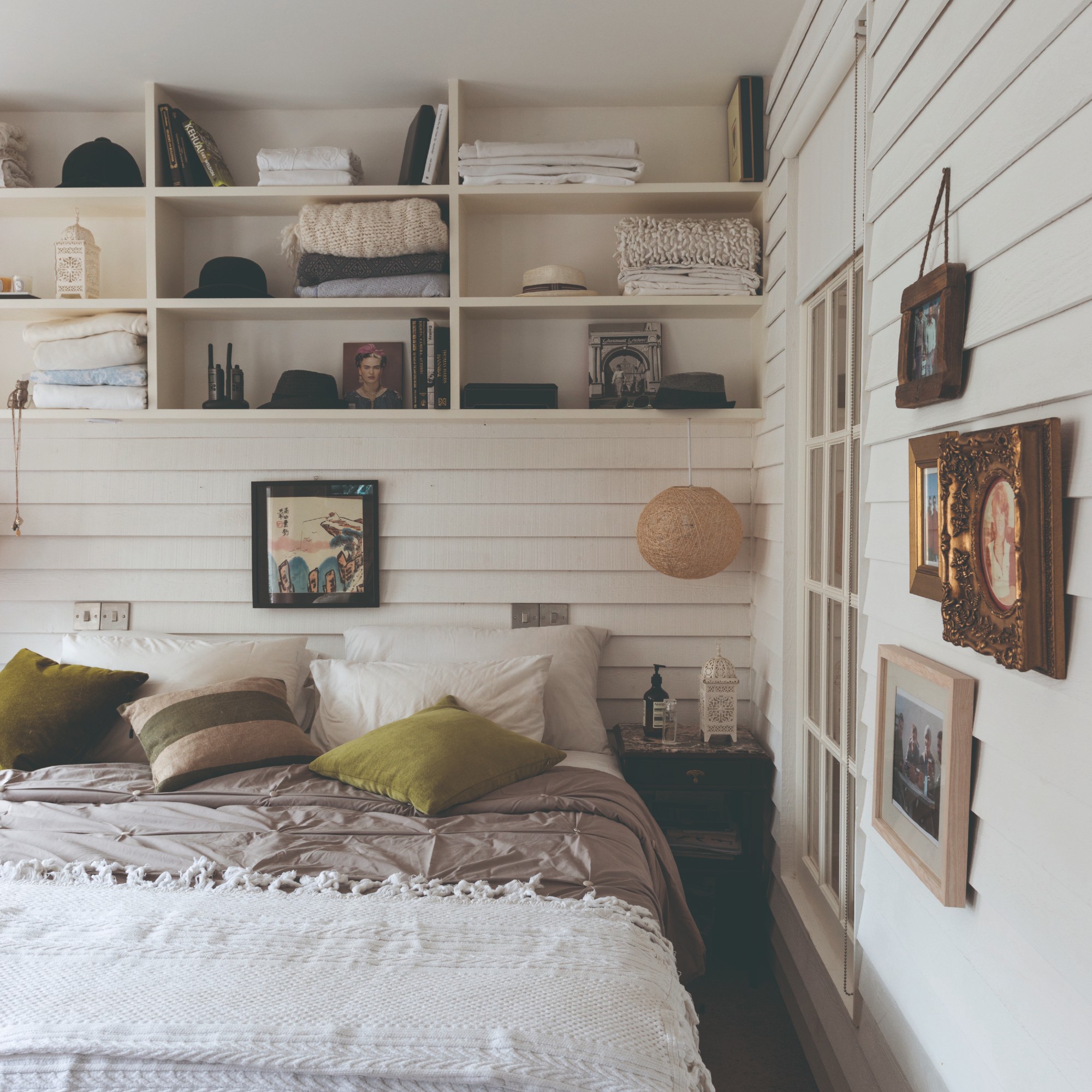 A white bedroom with panelled walls with open shelving and a gallery wall 