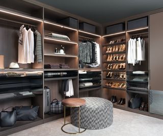 dark wood walk-in closet with shelf lighting and circular ottoman