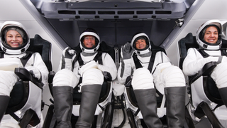 four people in white spacesuits inside a sleek white spacecraft cockpit