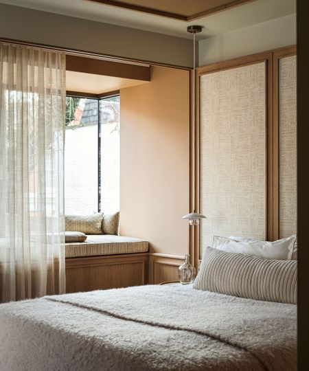 Warm neutral bedroom, a bed with a beige fluffy throw and a striped bolster cushion and a window seat with sheer drapes.
