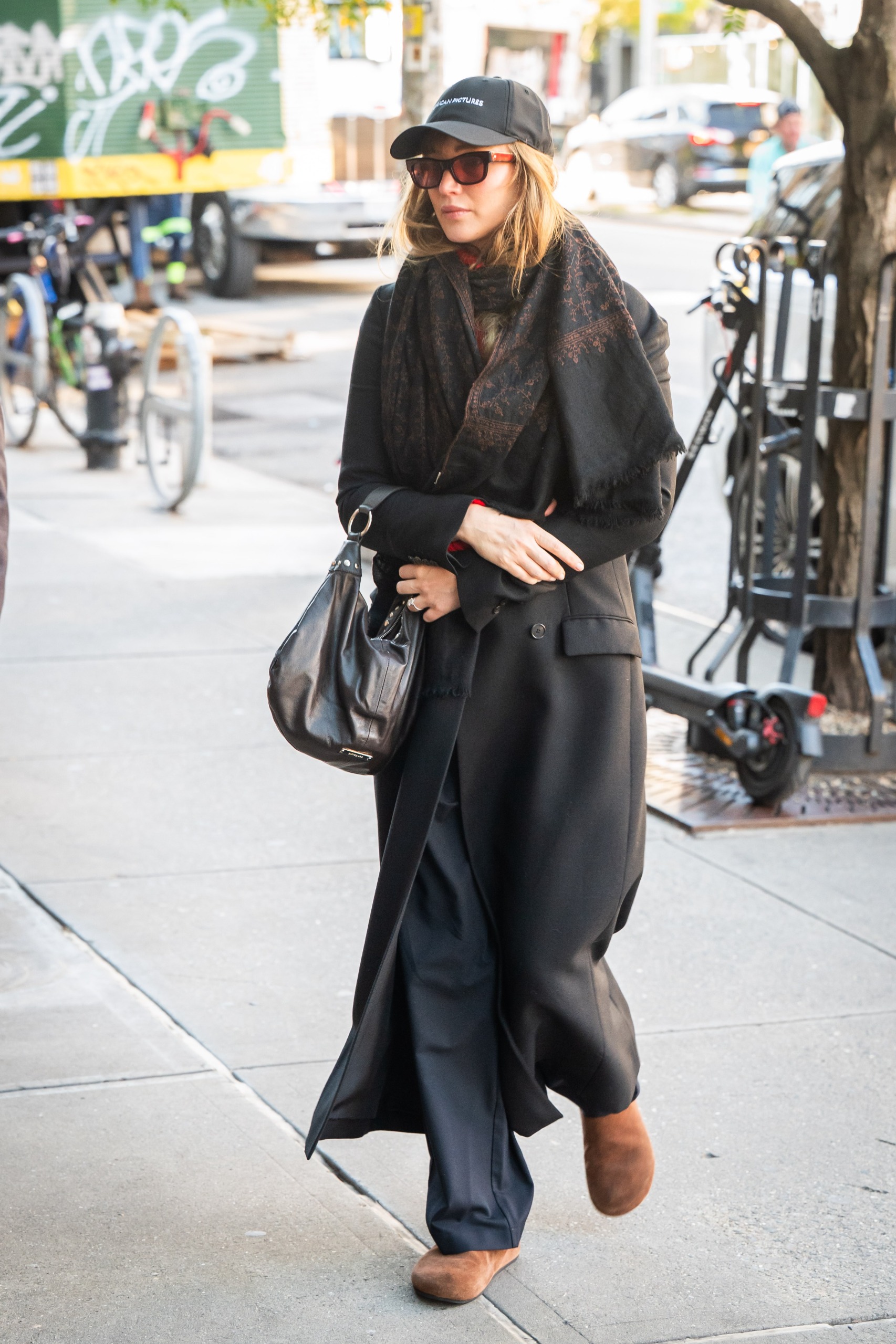 Jennifer Lawrence in New York City wearing a black coat with a paisley shawl scarf and brown suede mules.