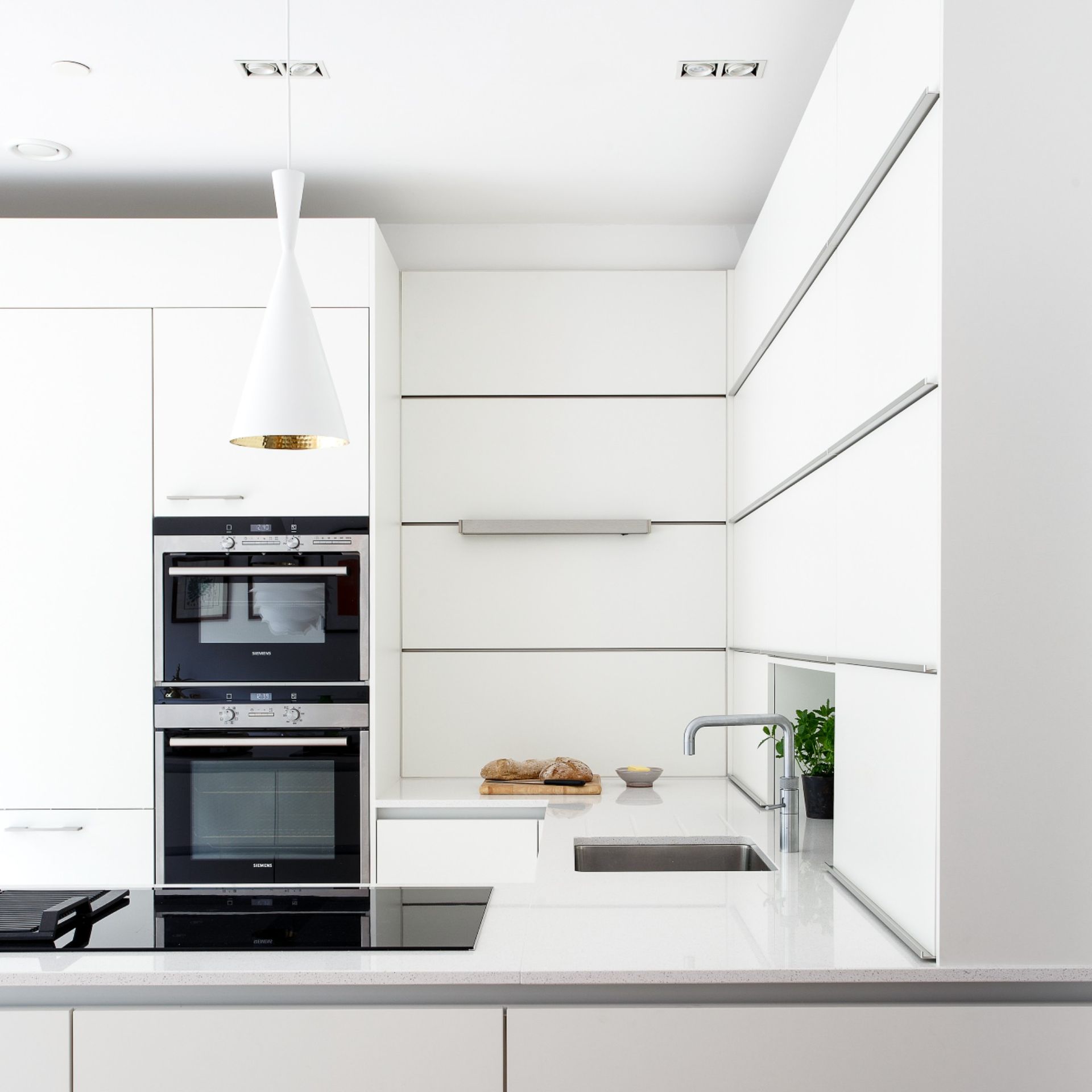 Kitchen with white countertops and pendant light, lots of white cabinets, black induction hob and double oven