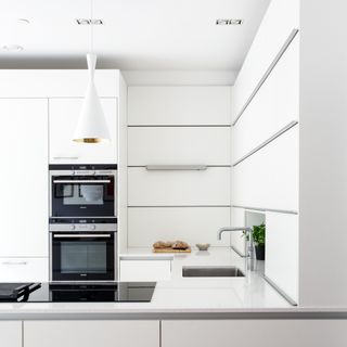 Kitchen with white counter tops and hanging lamp, lots of white cabinets, and black induction hob and twin oven